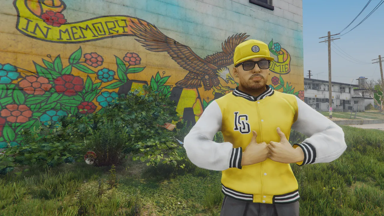 Vagos ped wearing a yellow varsity jacket, cap and sunglasses poses beside an In Memory mural in FiveM