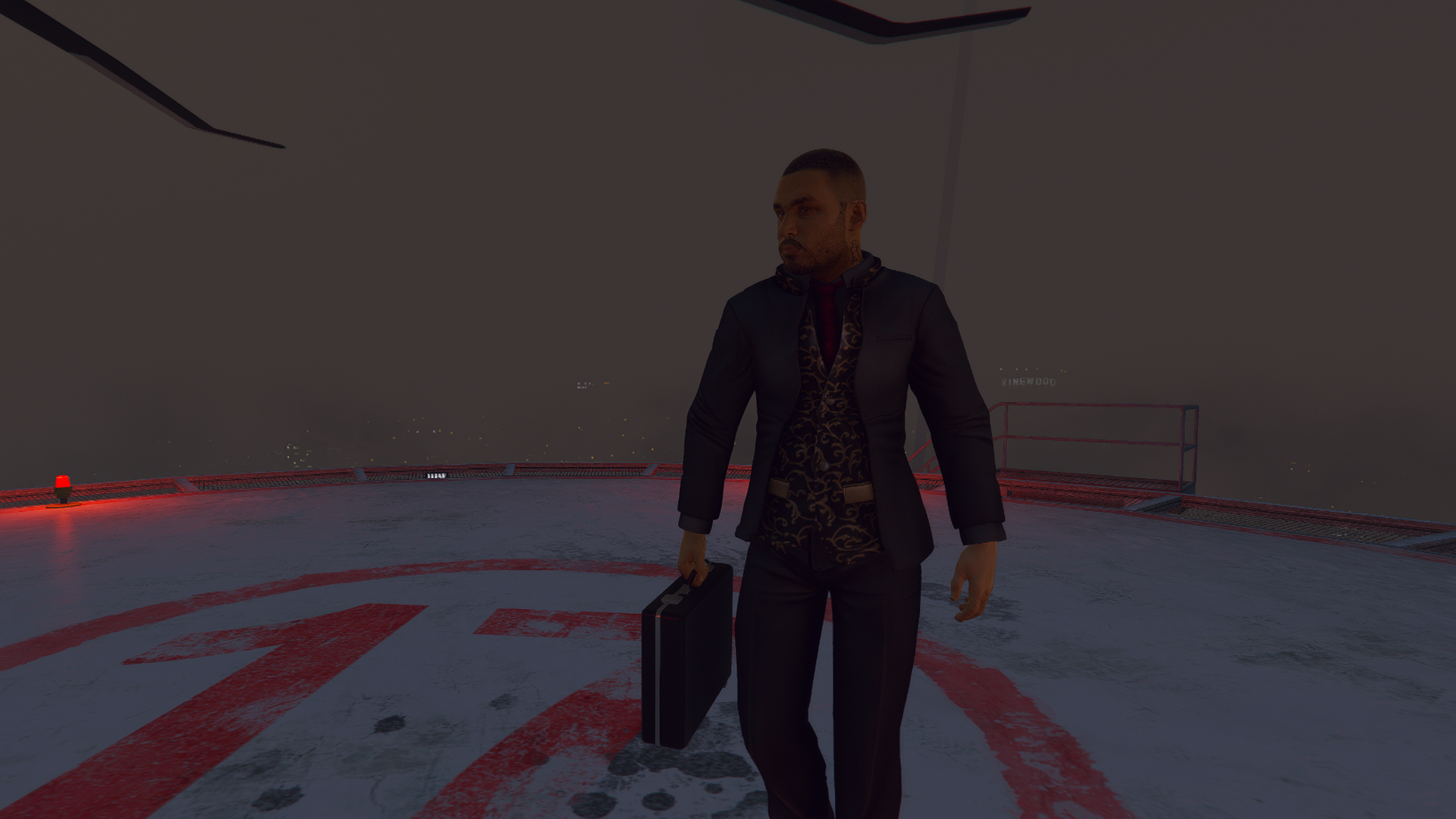 Vagos ped in a dark suit and patterned shirt carrying a briefcase across a helipad
