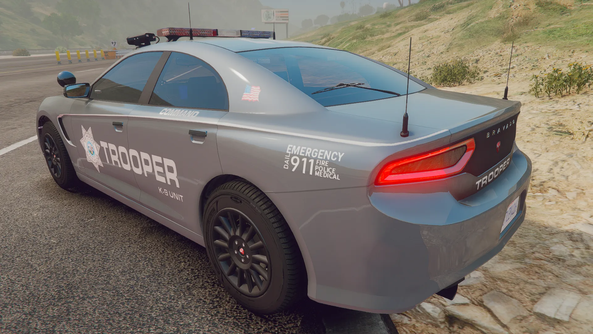 Police Buffalo V1 in grey Trooper K-9 unit livery with antennas, rear three-quarter view by a hillside road