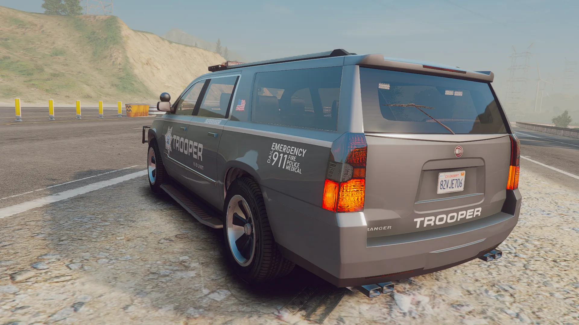 Police Granger V1 in grey Trooper livery, rear three-quarter view parked on a hillside highway shoulder