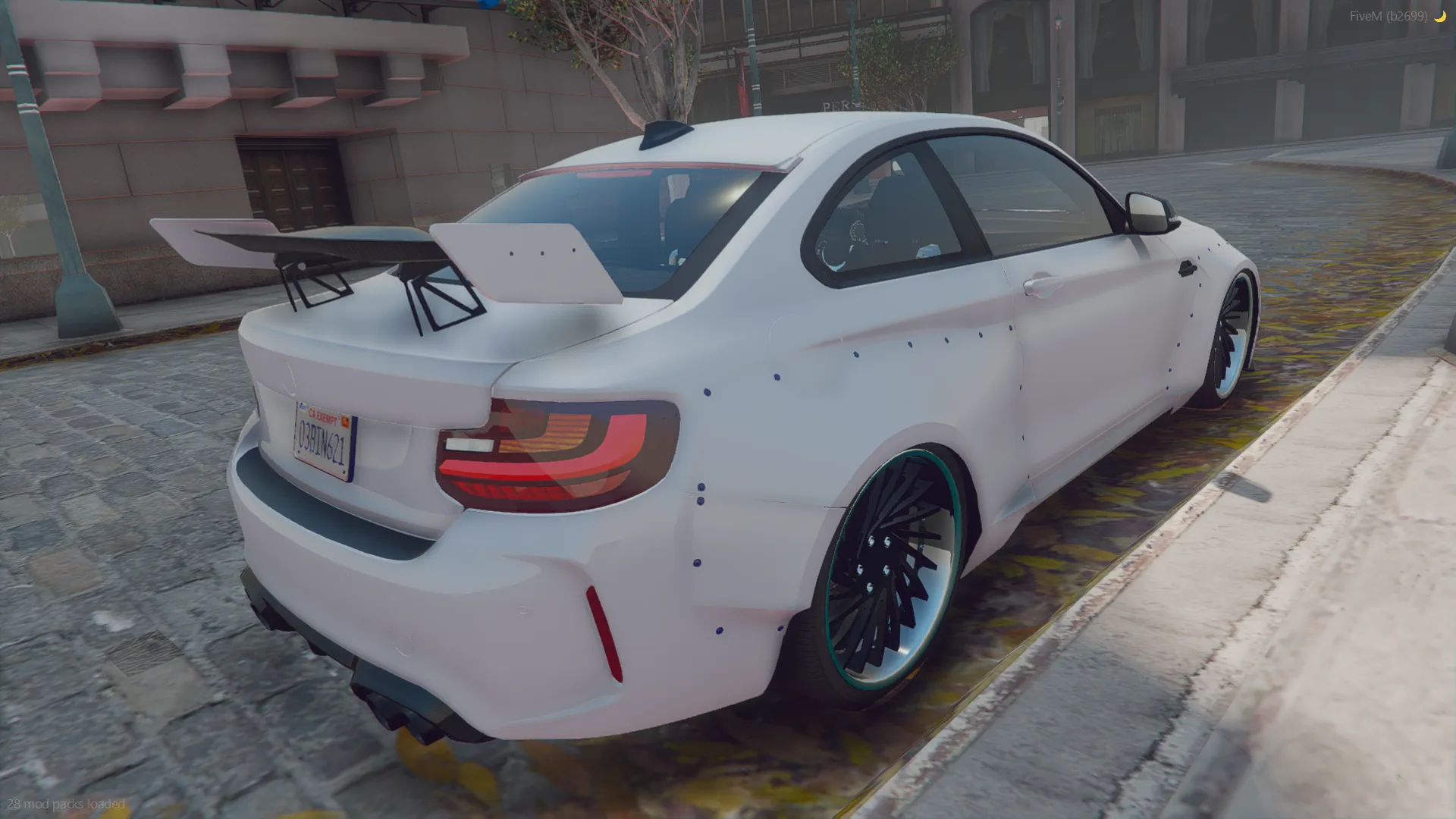 BMW M2 Competition 2018 rear three-quarter view with a tall rear wing and teal-lipped wheels by the curb